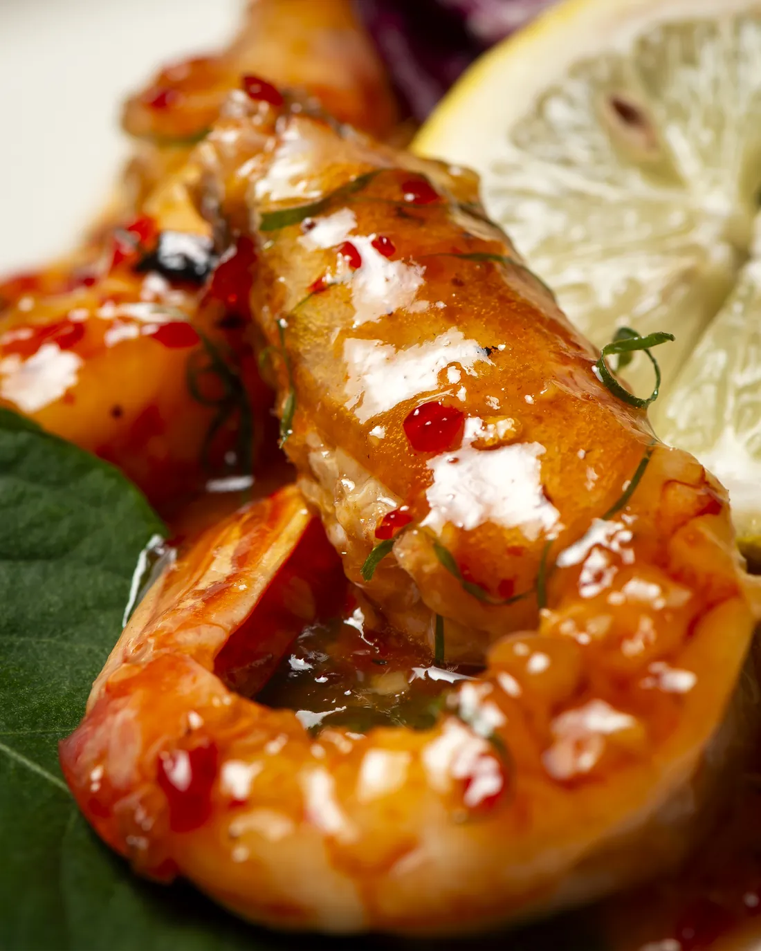 Glazed king prawns with pomegranate, next to a slice of lemon and green leaves