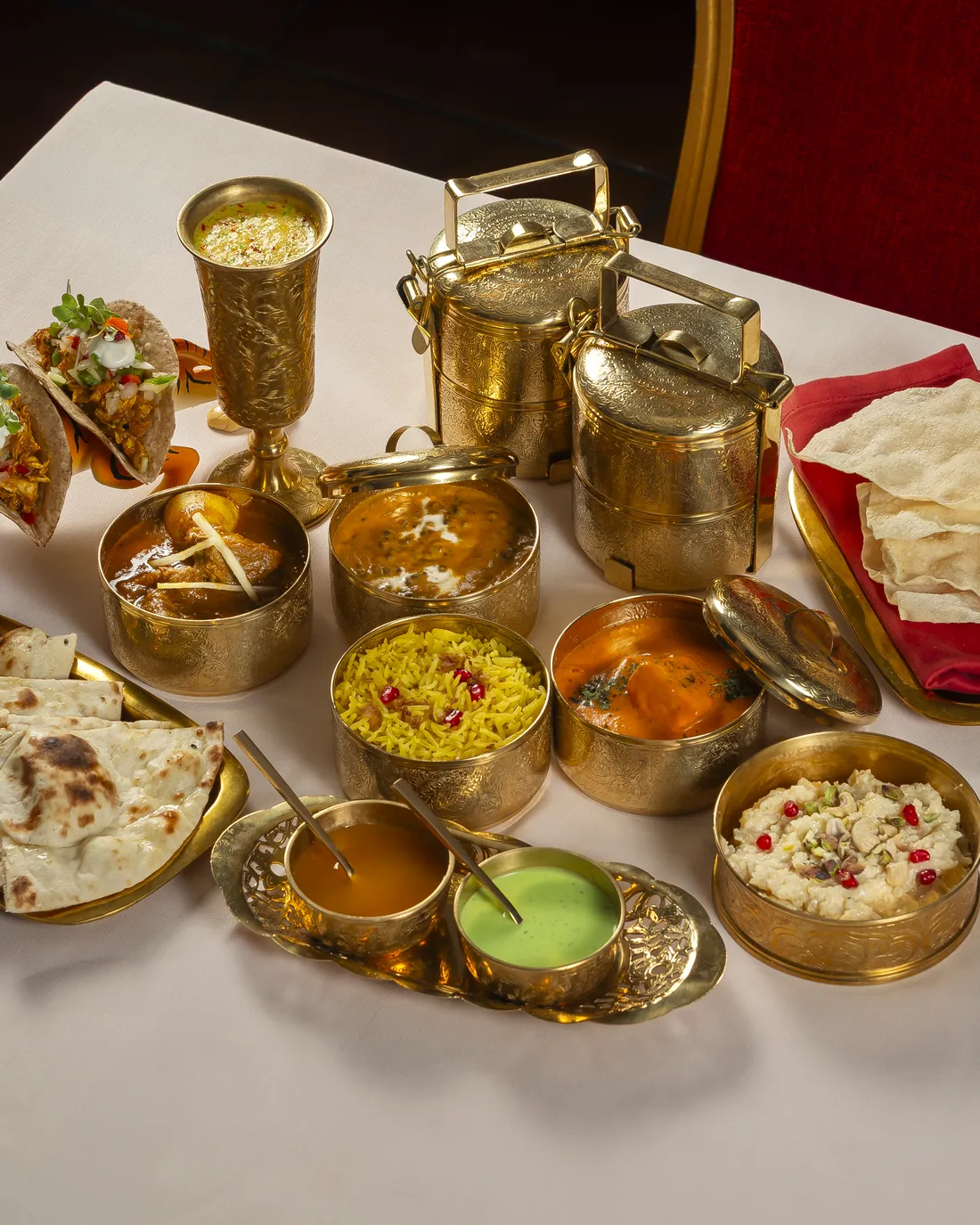 Brass bowls and tiffin tins with yellow rice, sauces and tacos, on the table