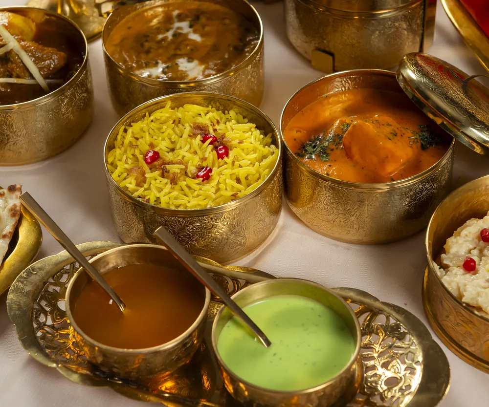 Brass bowls with yellow rice, curry, mint raita and sauces, served in the middle of the table