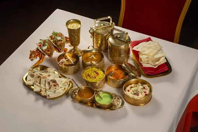 The Lunch box on the table: brass tiffin tins and bowls with curry, yellow rice, naan, poppadom, sauces, kheer and two Tiger tacos on a ceramic tiger