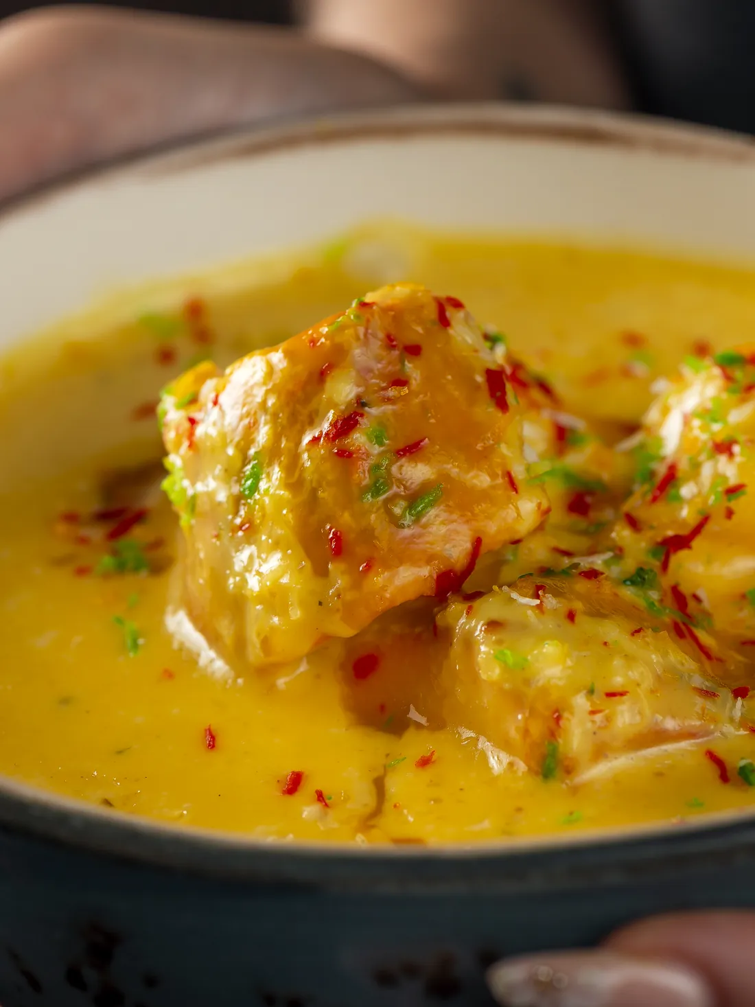 Mango chicken up close: pieces of chicken in a yellow sauce, with chilli flakes