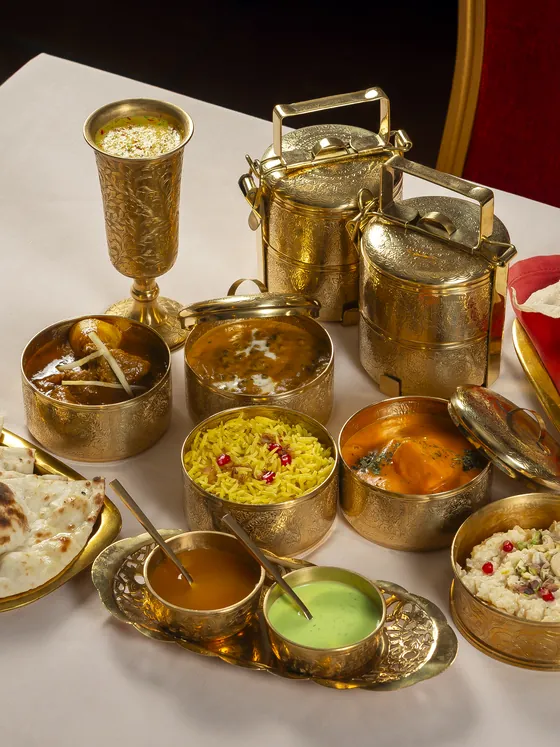 A table with brass tiffin tins and bowls: curry, yellow rice, naan and sauces