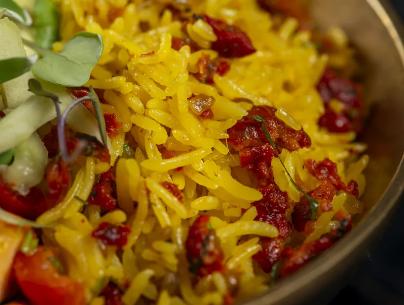 Yellow rice with red pepper, cucumber and sprouts, in a brass bowl