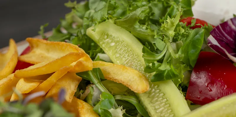 A green leaf salad with cucumber, red pepper and fried potatoes