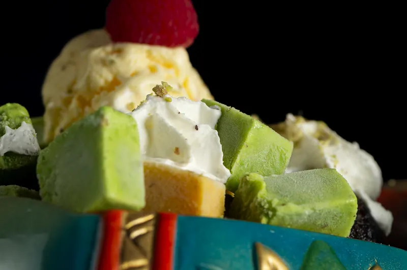 An ice cream dessert with a raspberry and green cubes of sweet